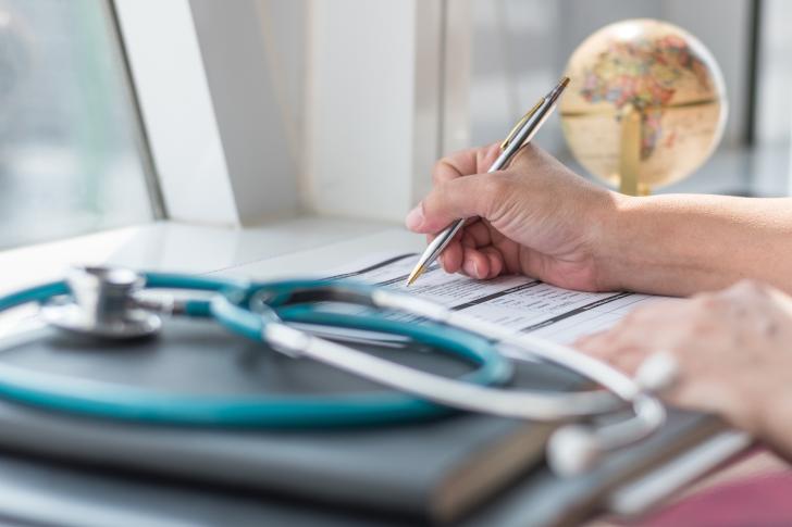 person filling out form with stethoscope next to them