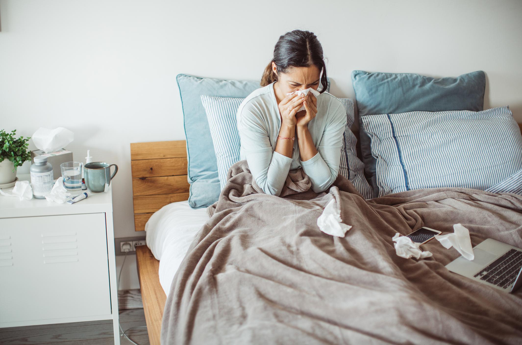 person in bed blowing nose, tissues on bed