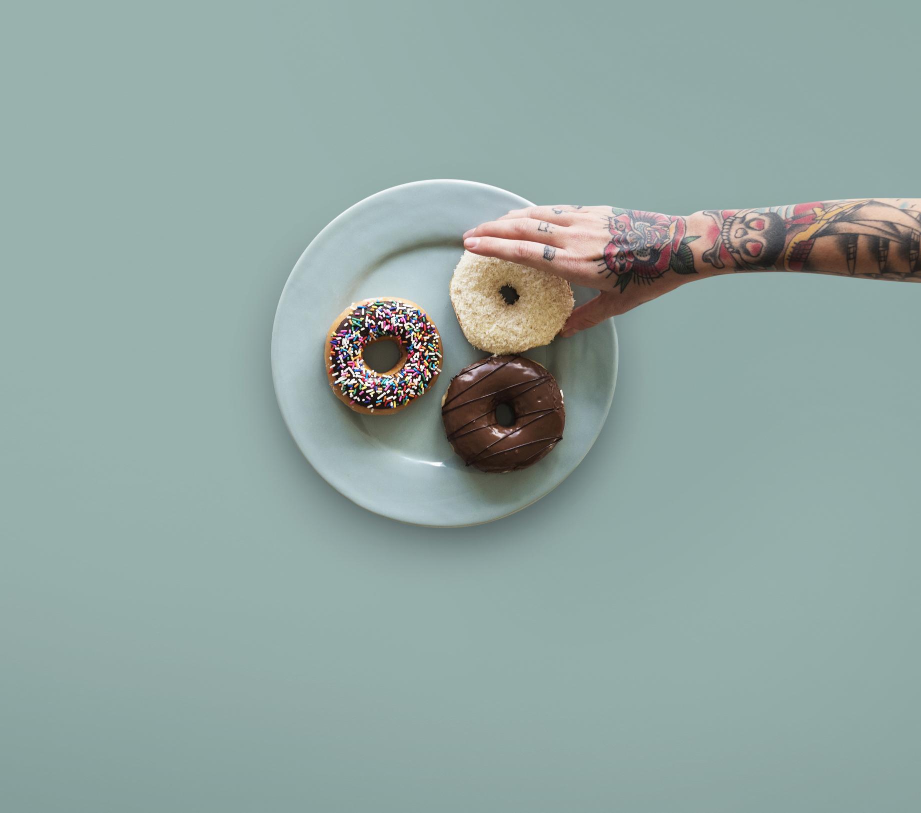 tattooed arm reaching for donut on a plate