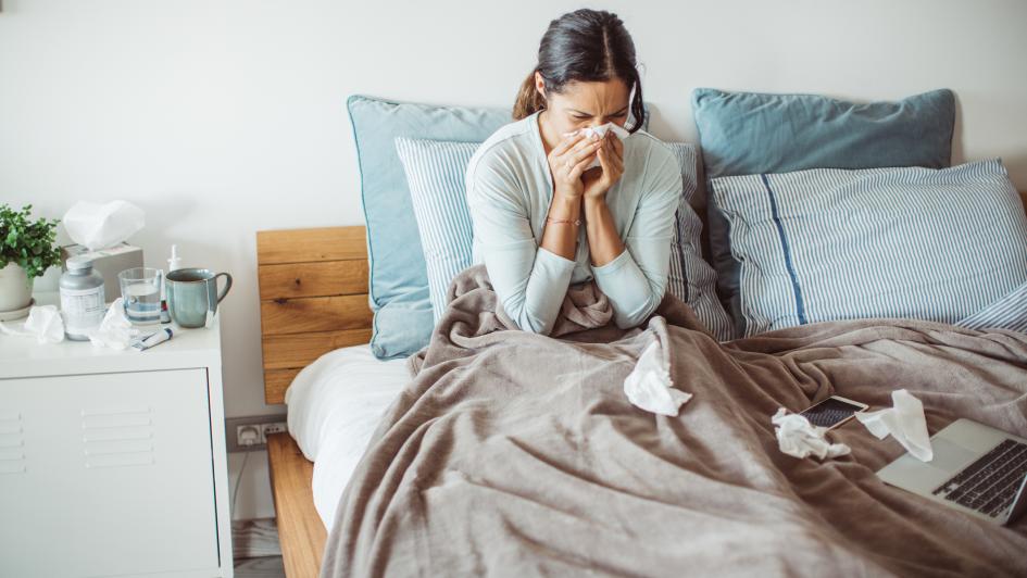 person in bed blowing nose, tissues on bed