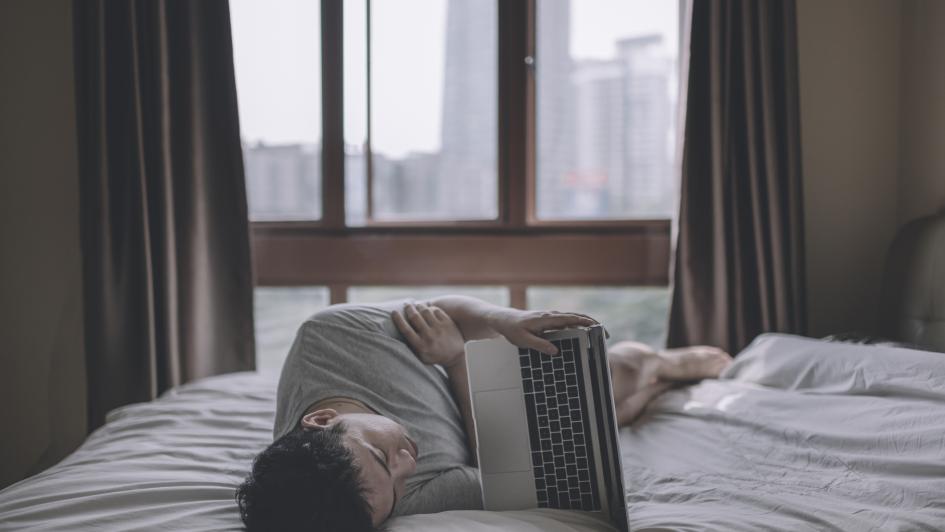 person laying on bed with laptop sideways