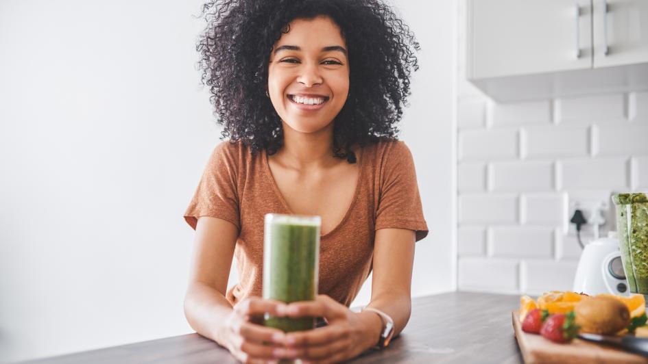 person standing at counter holding a glass of green juice