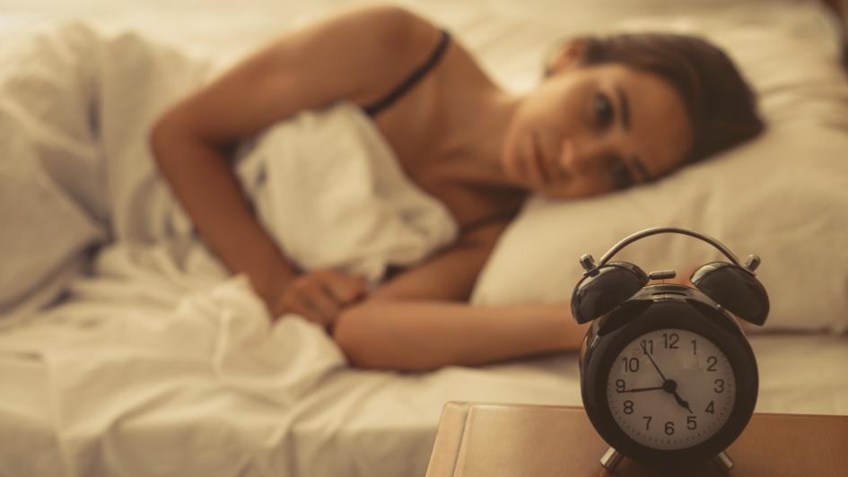 person laying in bed focusing on alarm clock