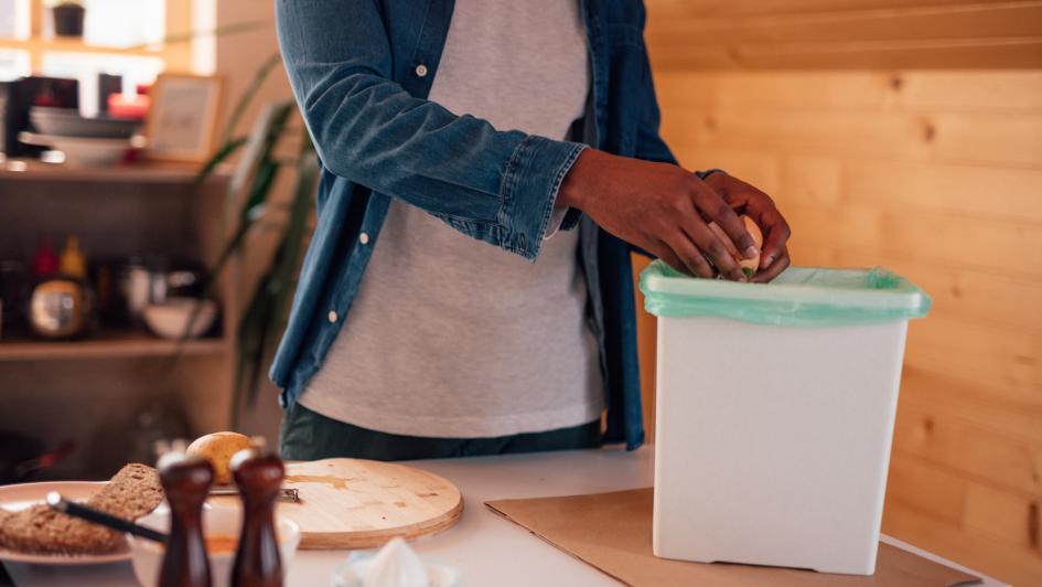 person putting trash in compost bin